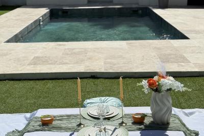 Table dressée avec vaisselle et fleurs bleues près d'une piscine entourée de dalles claires et de végétation.