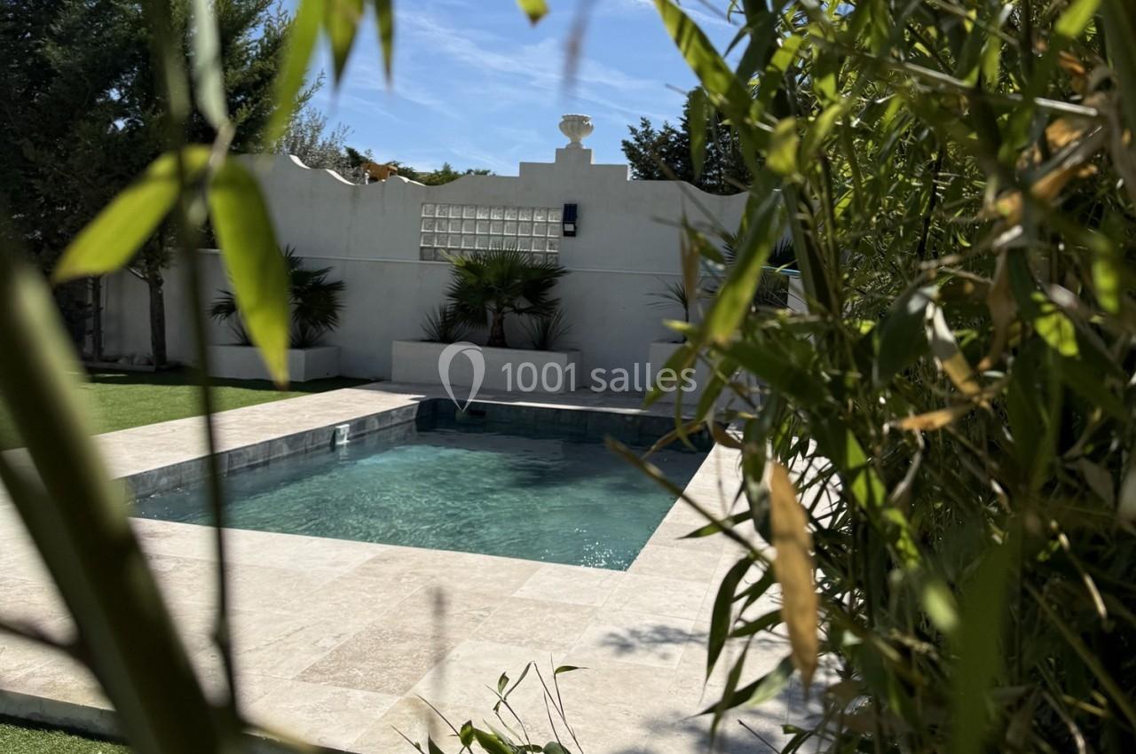Piscine extérieure entourée de végétation, avec un mur décoratif en arrière-plan sous un ciel dégagé.