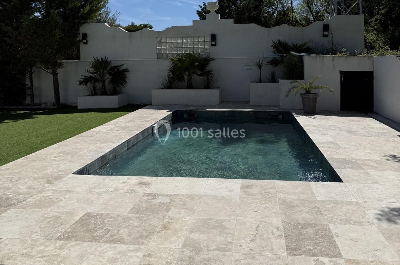 Piscine rectangulaire entourée de dalles claires, avec des plantes et un mur blanc en arrière-plan.