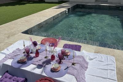 Table dressée avec vaisselle et fleurs bleues près d'une piscine entourée de dalles claires et de végétation.