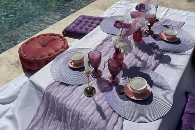 Table dressée avec vaisselle et fleurs bleues près d'une piscine entourée de dalles claires et de végétation.