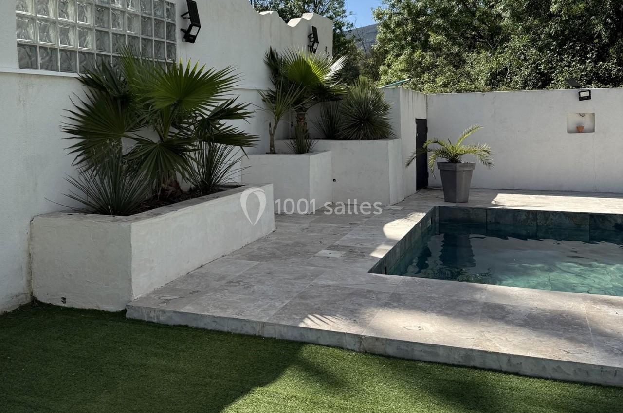 Piscine entourée de dalles en pierre, avec des plantes en pots et un mur blanc en arrière-plan.