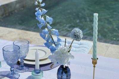 Table dressée avec vaisselle et fleurs bleues près d'une piscine entourée de dalles claires et de végétation.