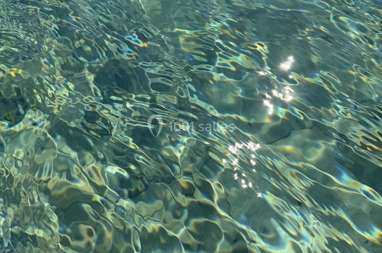 Reflets du soleil sur une surface d'eau claire avec des ondulations et des nuances de bleu et vert.