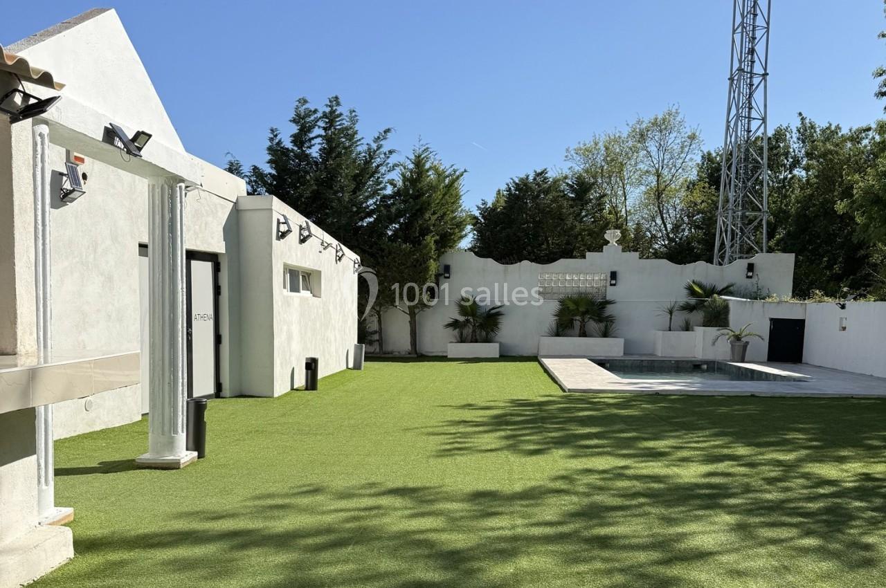 Jardin avec pelouse synthétique, petite piscine, murs blancs et arbres en arrière-plan sous un ciel dégagé.