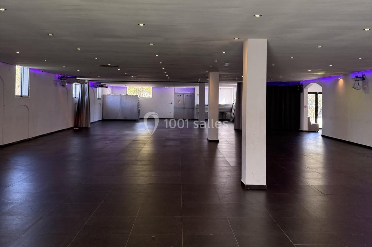 Salle spacieuse avec sol en carrelage sombre, murs blancs, éclairage au plafond et lumières violettes en périphérie.