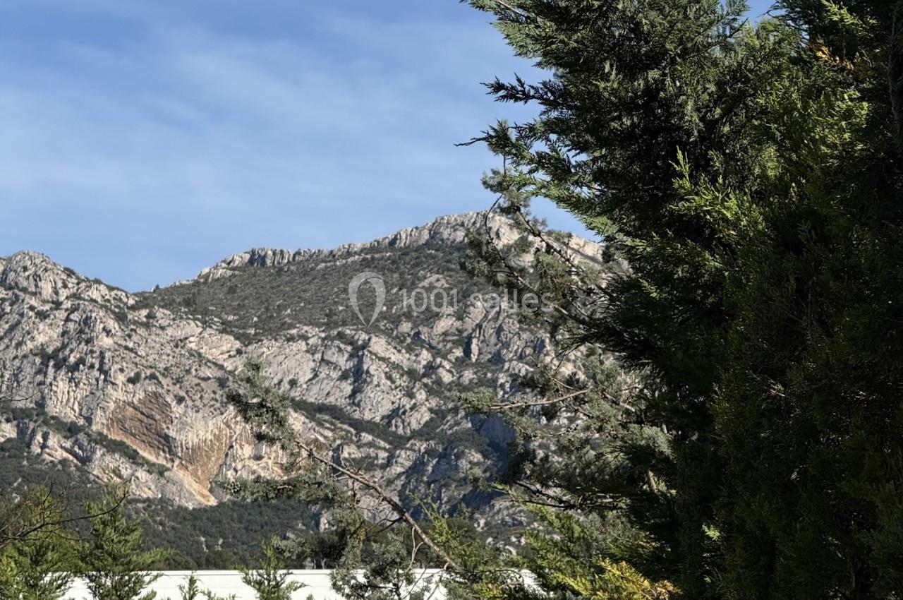 Paysage de montagne rocheuse sous un ciel bleu, avec des arbres verts au premier plan.