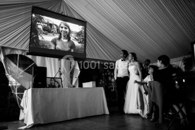 Salle décorée avec des ballons blancs et dorés, rangées de chaises rouges alignées sur un tapis rouge.