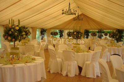 Salle décorée avec des ballons blancs et dorés, rangées de chaises rouges alignées sur un tapis rouge.