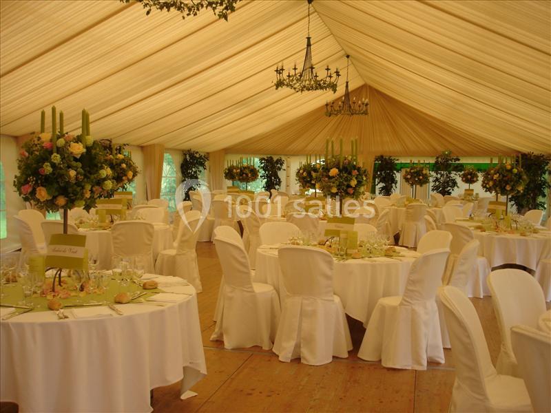 Salle de réception décorée avec des tables rondes, nappes blanches, chandeliers et arrangements floraux.