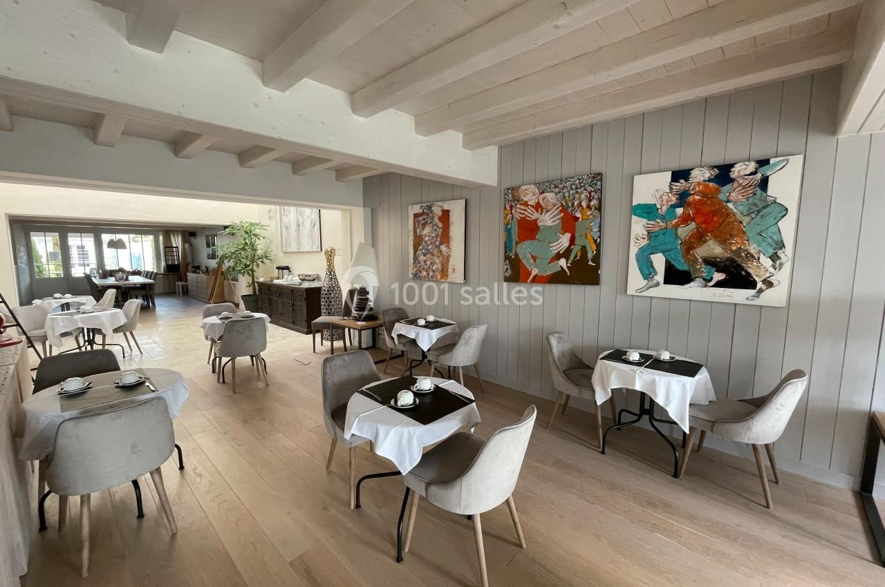 Salle de restaurant lumineuse avec tables dressées, chaises modernes et peintures colorées accrochées aux murs.