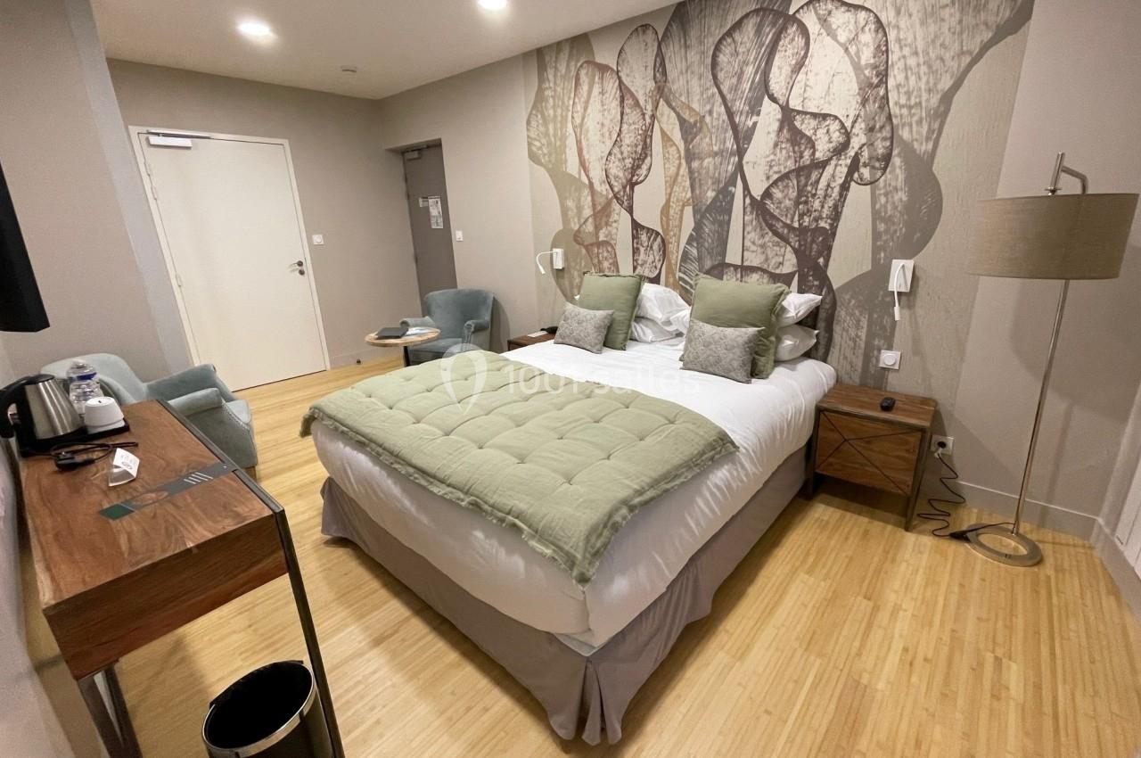 Chambre d'hôtel moderne avec lit double, bureau en bois, fauteuils, lampadaire et décoration murale abstraite.