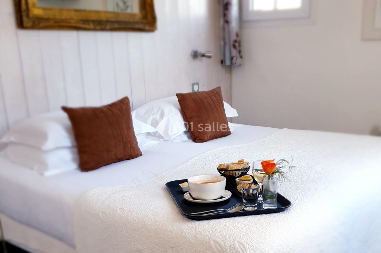 Plateau petit-déjeuner avec tasse, jus et viennoiseries posé sur un lit blanc dans une chambre lumineuse.