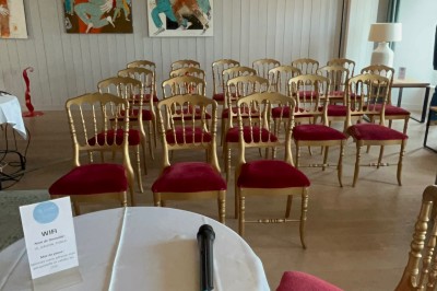 Salle de réunion avec des chaises dorées à assise rouge, une table ronde au premier plan et des tableaux accrochés au mur.