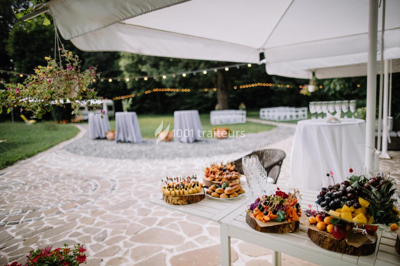 Buffet en plein air avec des fruits et amuse-bouches sur des tables, sous des parasols blancs, dans un jardin éclairé.
