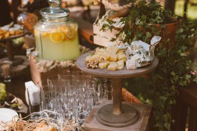 Plateau en bois avec fromages variés, noix et raisins, entouré de verres et d'une jarre de citronnade en arrière-plan.