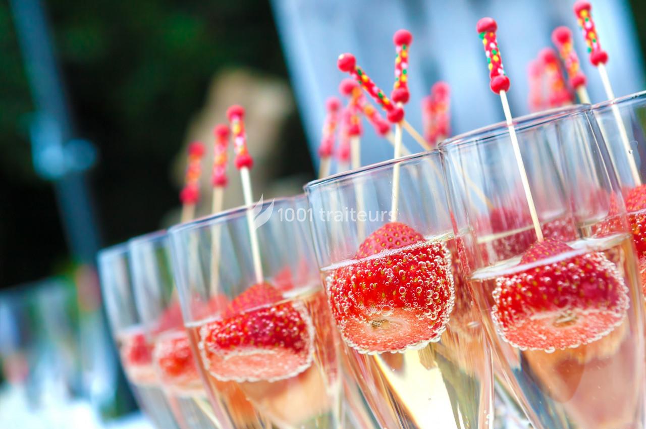 Verres de champagne garnis de fraises et de bâtonnets décoratifs alignés sur une table.