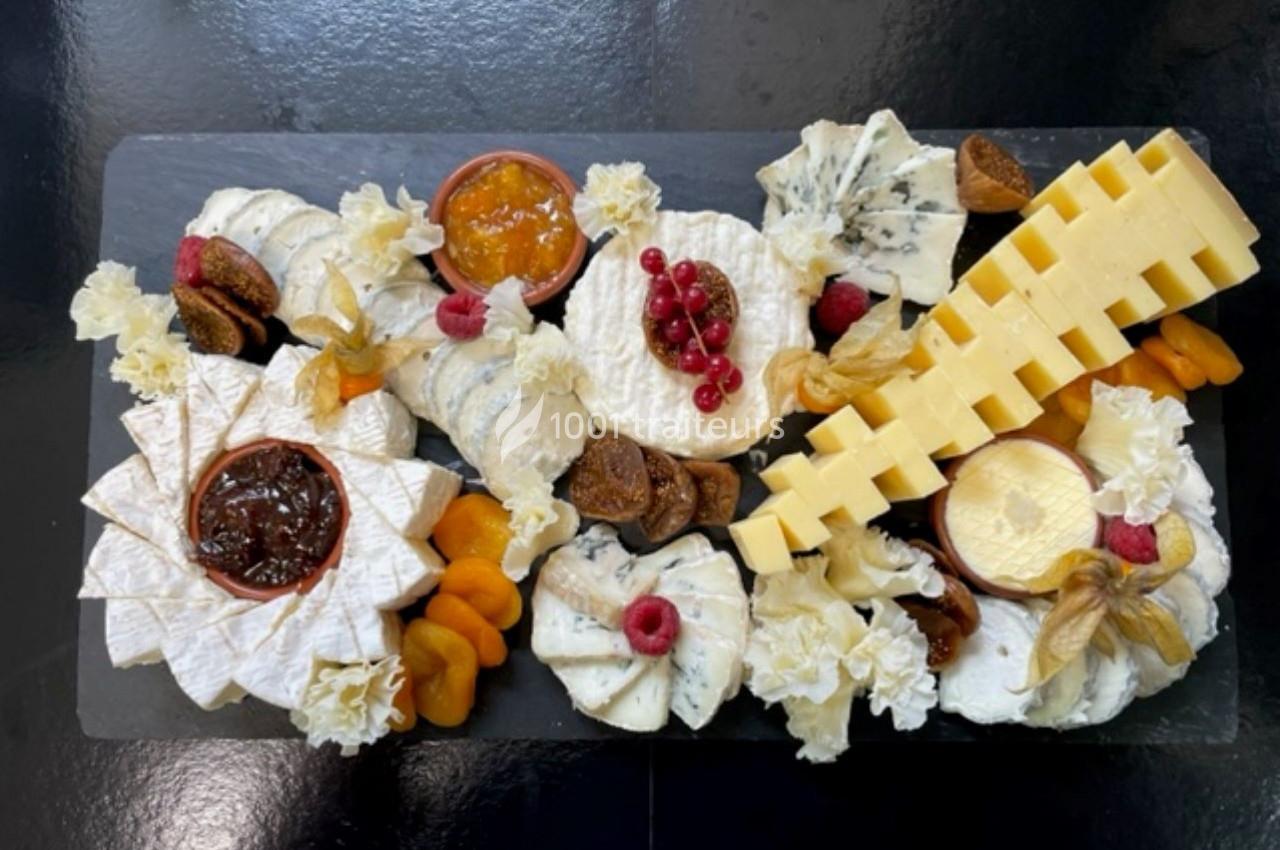 Plateau de fromages variés avec fruits secs, confitures et décorations sur une ardoise noire.