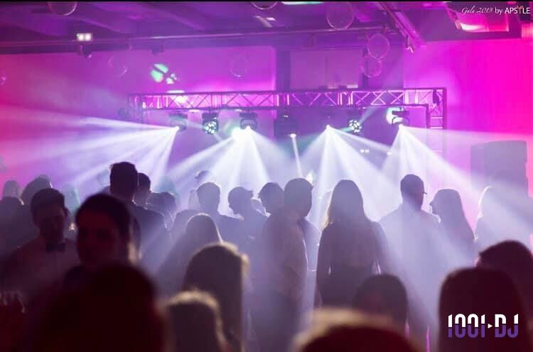 Personnes dansant dans une salle éclairée par des projecteurs et des lumières colorées.