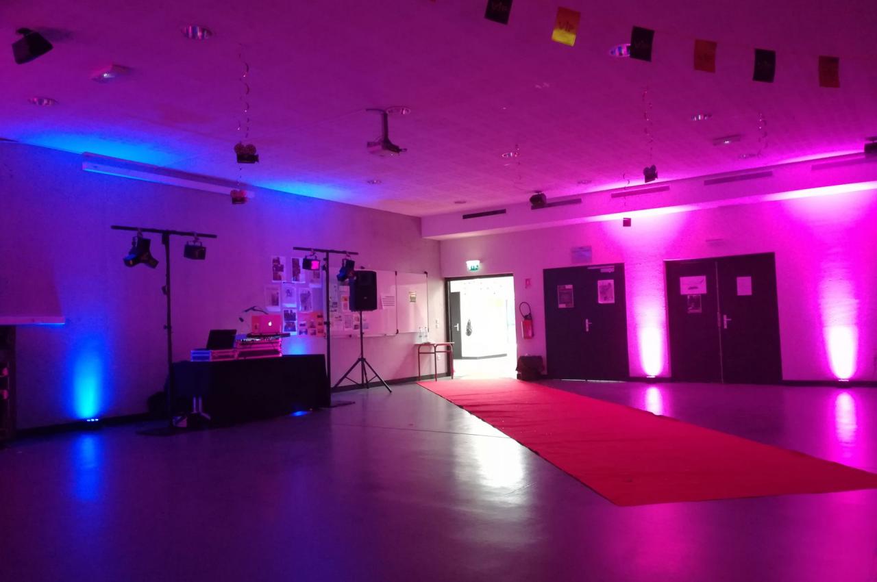 Salle décorée avec éclairage coloré, tapis rouge au sol, matériel de sonorisation et affiches sur les murs.