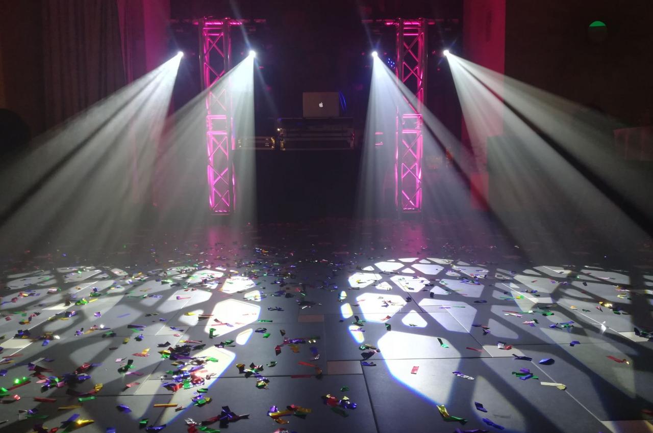 Piste de danse éclairée par des projecteurs colorés, avec des confettis éparpillés au sol.