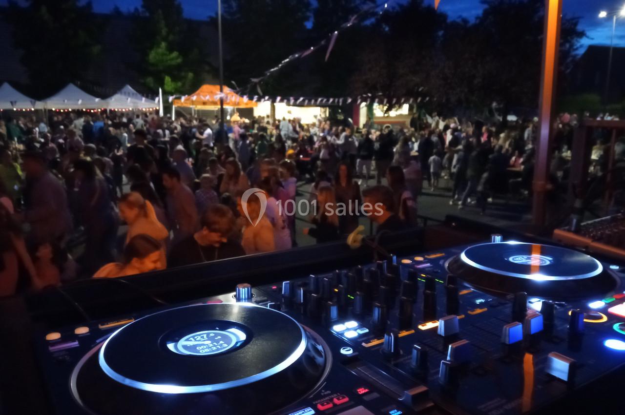Vue d'une table de mixage en premier plan avec une foule rassemblée lors d'un événement nocturne en extérieur.