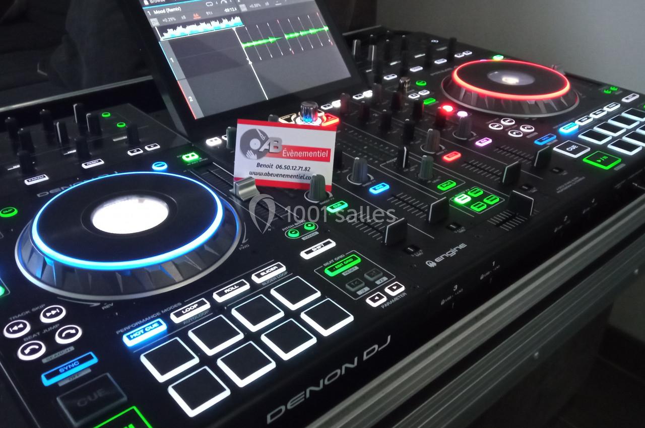 Table de mixage Denon DJ avec éclairages colorés, écran tactile et carte de visite posée au centre.