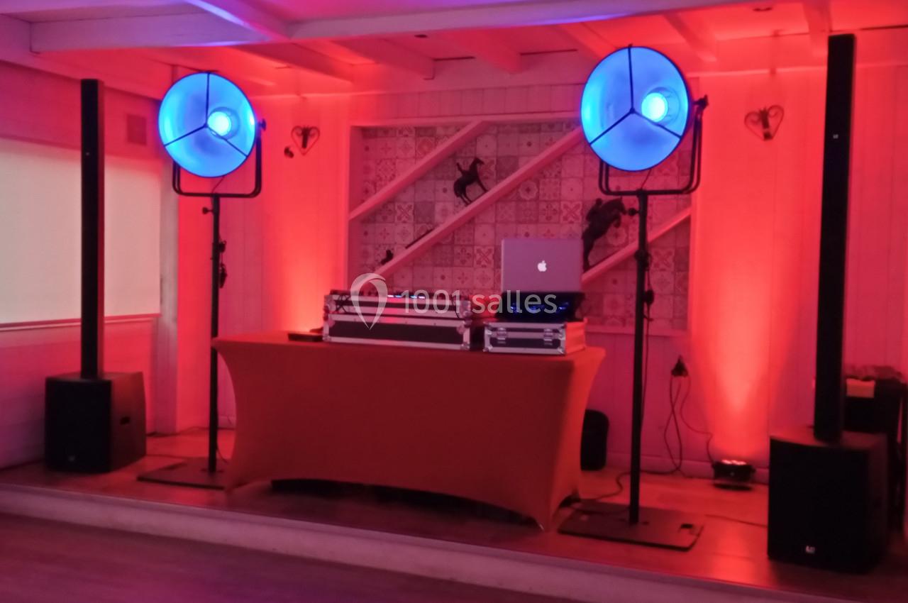 Équipement de DJ avec table de mixage, ordinateur portable et éclairage bleu dans une salle à la décoration chaleureuse.