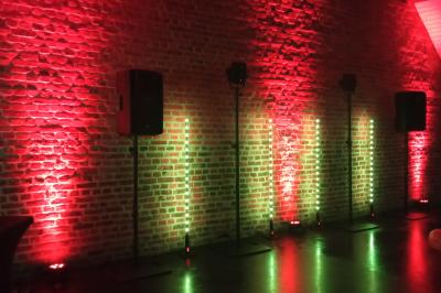 Mur en briques éclairé par des lumières rouges et vertes avec des enceintes noires sur pieds alignées.