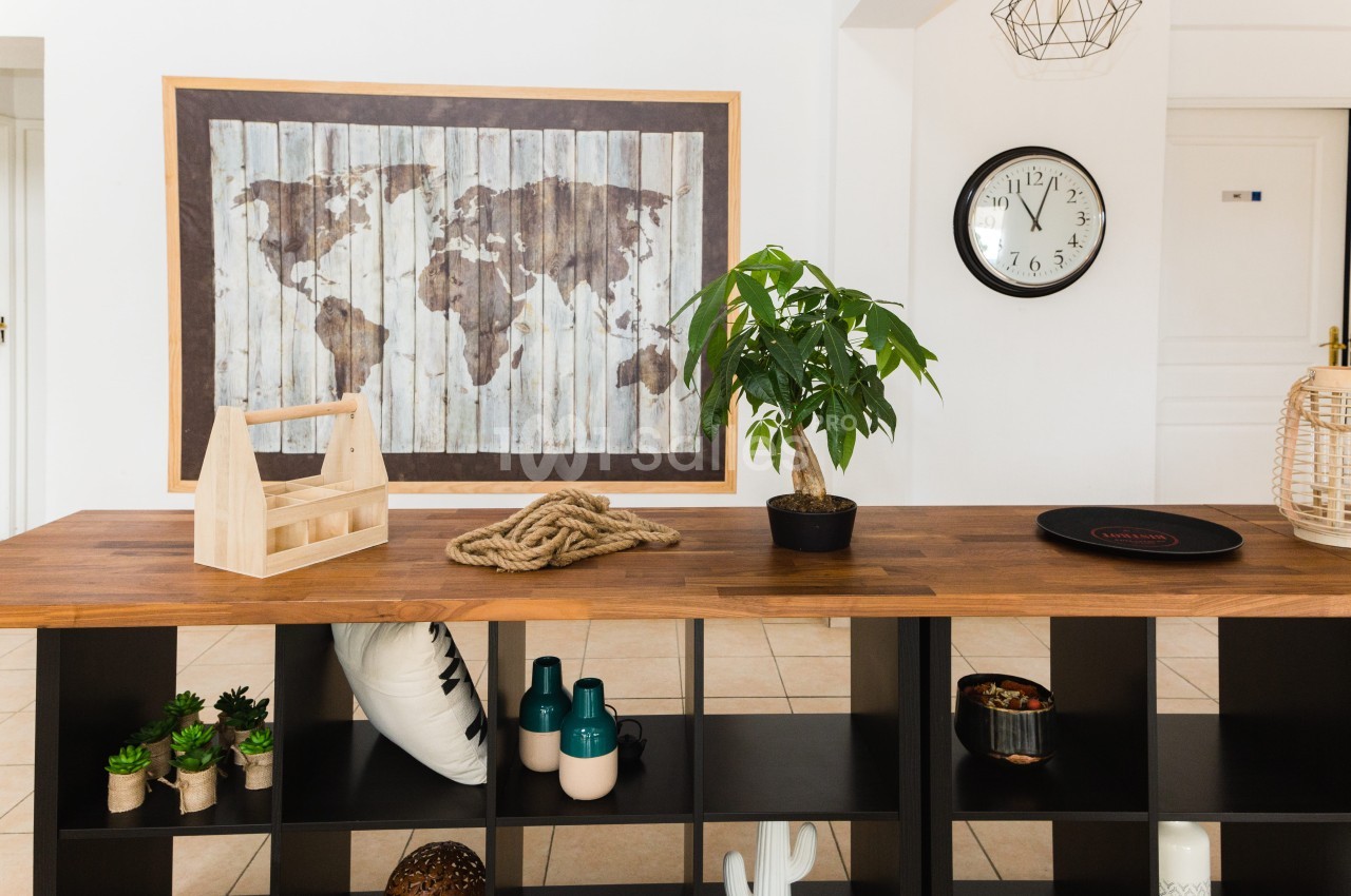 Comptoir en bois sombre garni d'une carte du monde murale, d'un bonsaï, d'une horloge et de petits objets décoratifs, sur fond de mur blanc.