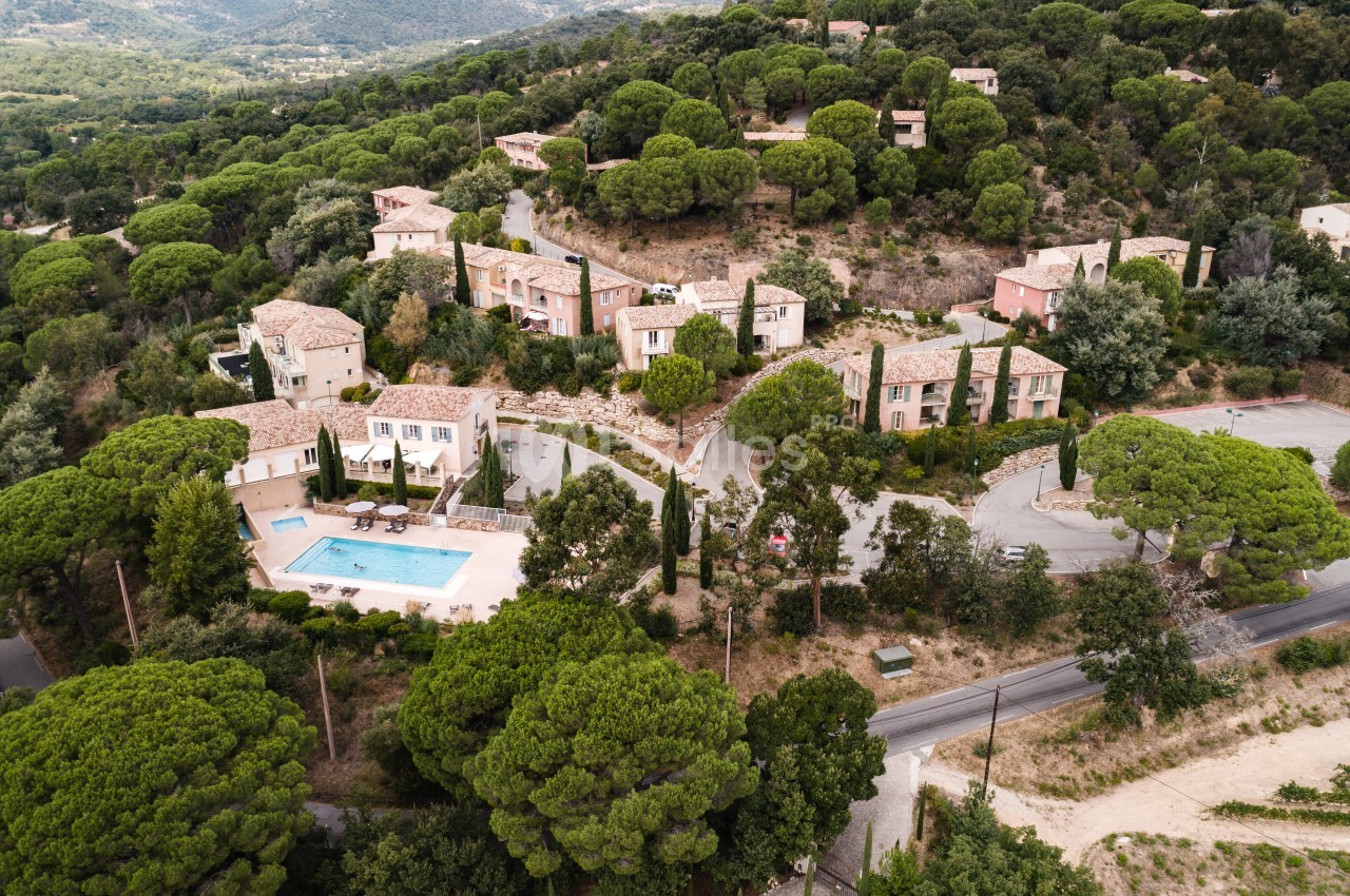 Vue aérienne d'un ensemble de maisons méditerranéennes aux toits de tuiles et façades roses, avec une piscine extérieure entourée de transats, au milieu d'une végétation de pins parasols. Hmm, "Vue" en début est interdit. Reformulons. Ensemble de maisons