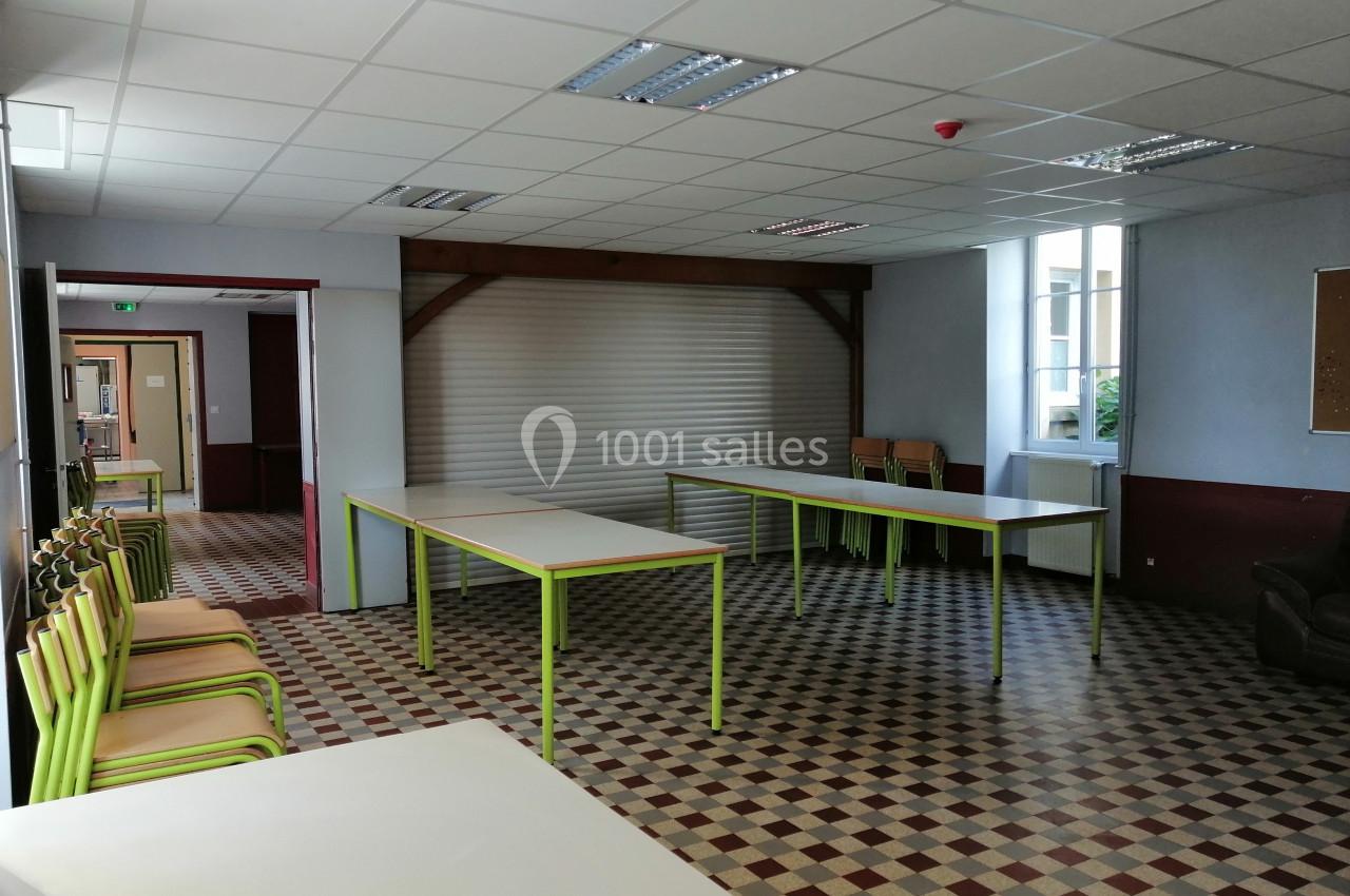 Salle vide avec tables et chaises empilées, sol en carrelage à motifs et lumière naturelle entrant par les fenêtres.