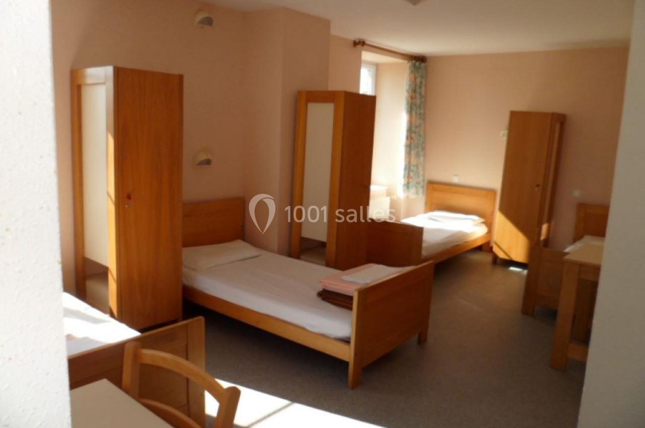 Chambre lumineuse avec plusieurs lits simples, armoires en bois et une fenêtre avec rideaux fleuris.