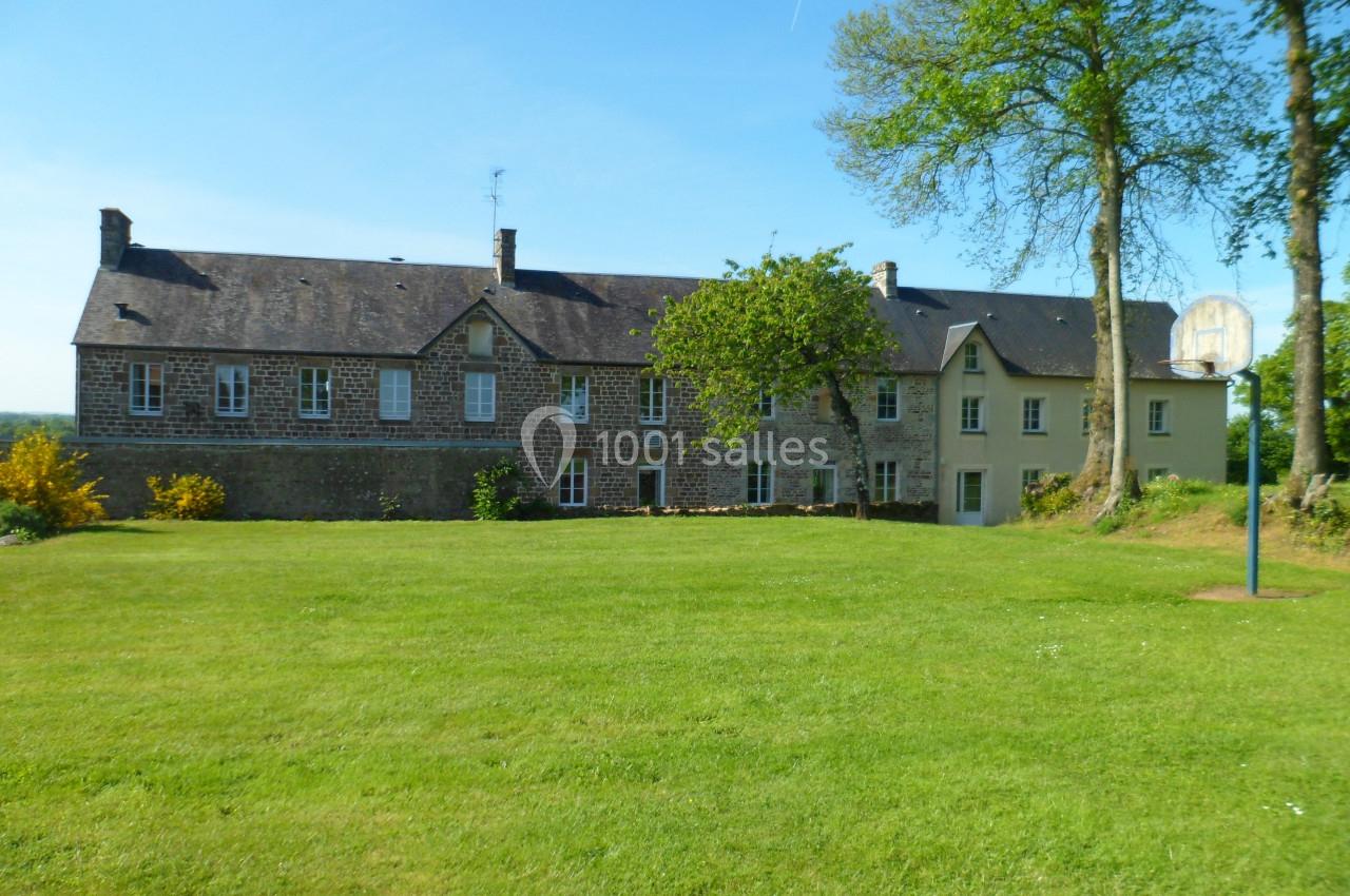 Bâtiment en pierre avec toit en ardoise, entouré d'une pelouse et d'arbres sous un ciel dégagé.
