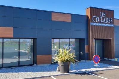 Parking extérieur avec marquages au sol, quelques voitures stationnées, bâtiments et champs en arrière-plan.