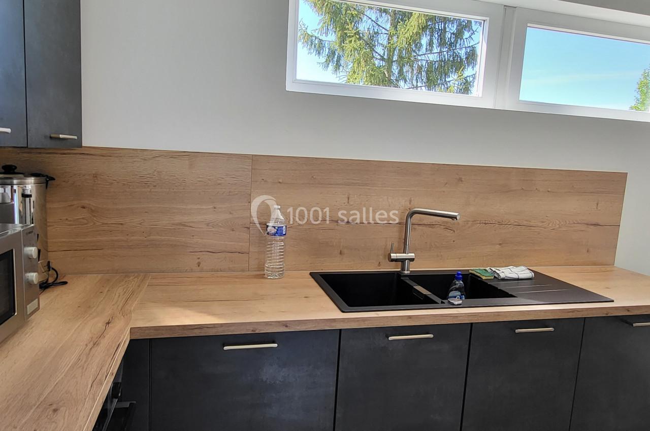 Cuisine moderne avec plan de travail en bois, évier noir, micro-ondes et fenêtre laissant entrer la lumière naturelle.