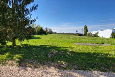 Parking extérieur avec marquages au sol, quelques voitures stationnées, bâtiments et champs en arrière-plan.