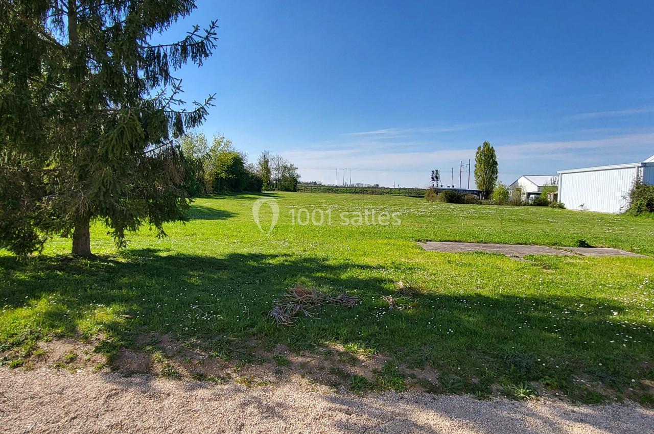 Un grand espace vert avec pelouse, un arbre, des bâtiments en arrière-plan et un ciel dégagé.