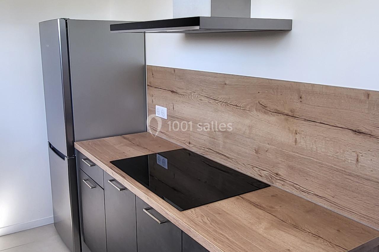 Cuisine moderne avec plan de travail en bois, plaques de cuisson noires, hotte en inox et réfrigérateur argenté.