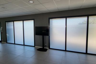 Parking extérieur avec marquages au sol, quelques voitures stationnées, bâtiments et champs en arrière-plan.