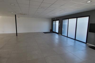 Parking extérieur avec marquages au sol, quelques voitures stationnées, bâtiments et champs en arrière-plan.