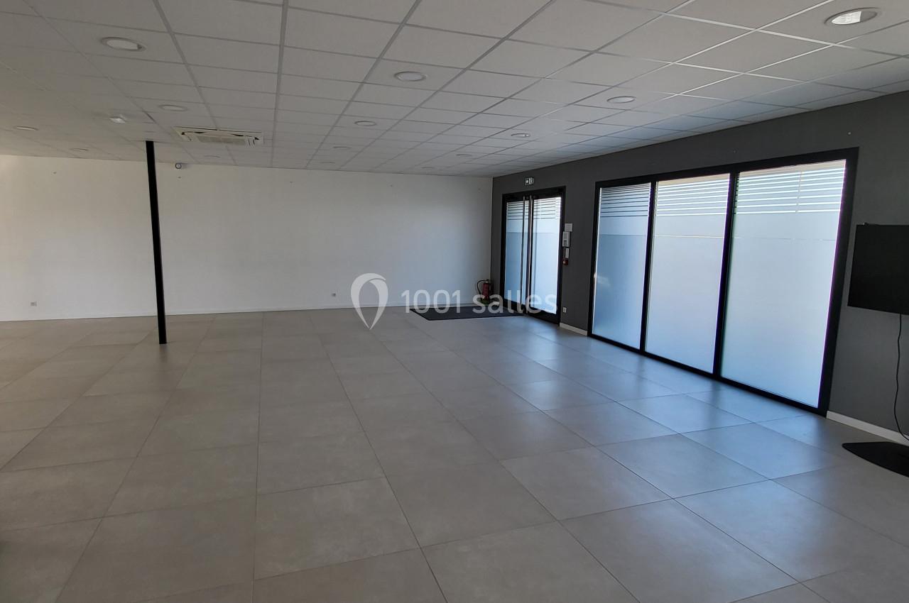 Salle vide avec carrelage clair, murs blancs, plafond à dalles, grandes baies vitrées et un écran sur pied.