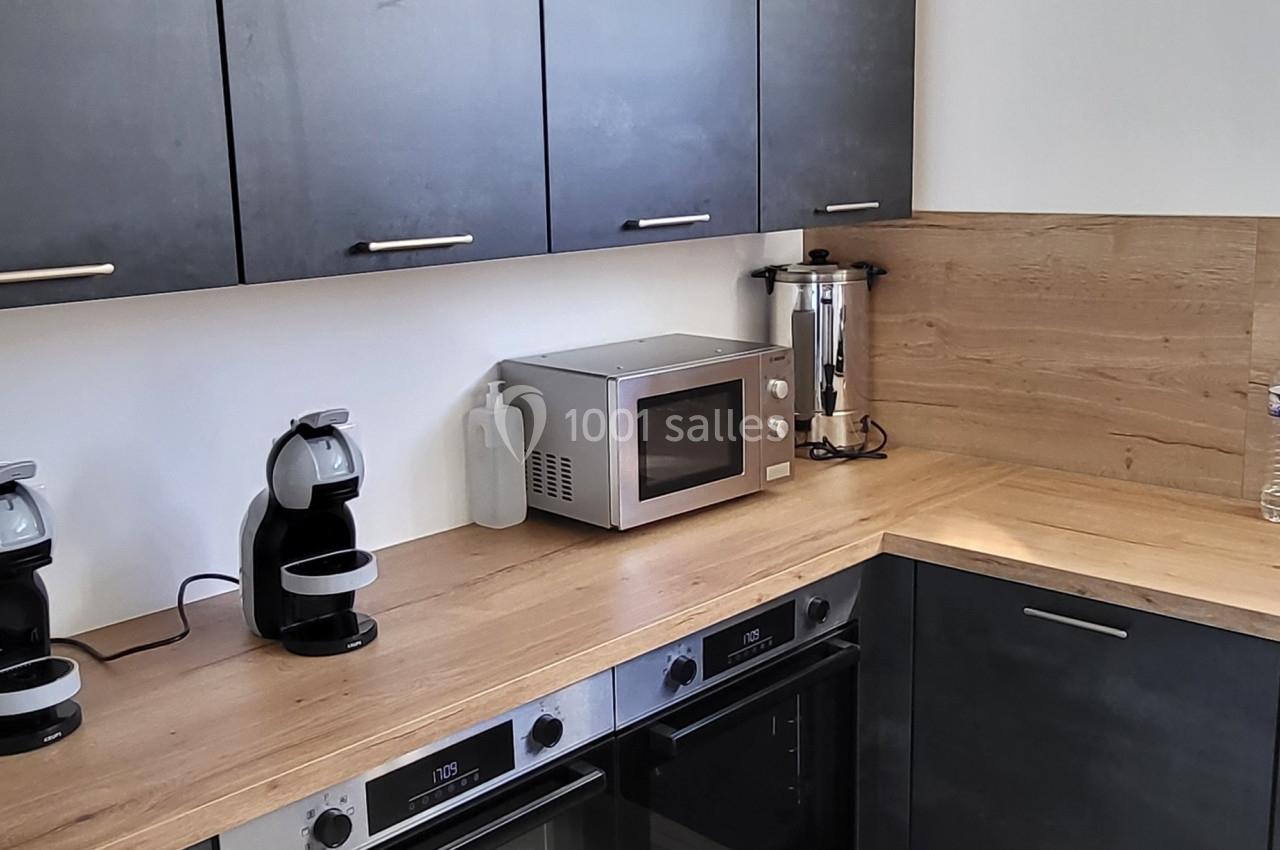 Cuisine moderne avec meubles noirs, plan de travail en bois clair, électroménager intégré et carrelage beige au sol.