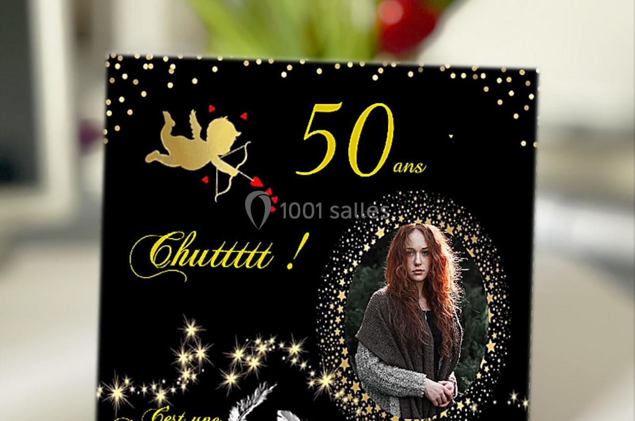 Carte d'anniversaire noire avec décorations dorées, photo d'une femme et texte annonçant une surprise pour 50 ans.