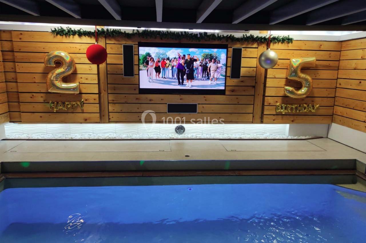 Piscine intérieure avec écran mural, décorations d'anniversaire ’25’ dorées et boules suspendues.