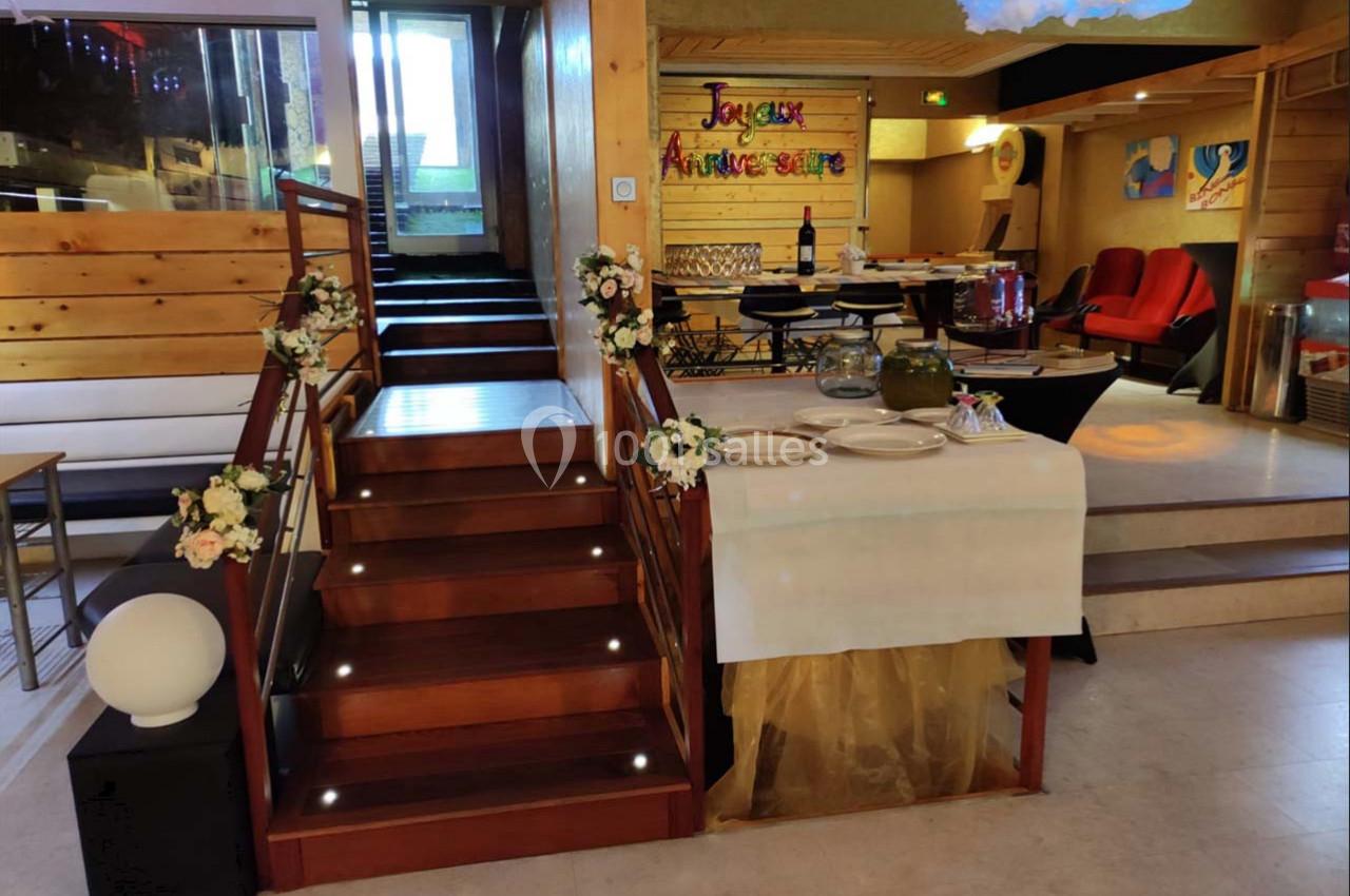 Escalier en bois décoré de fleurs, table dressée avec vaisselle et buffet, panneau ’Joyeux Anniversaire’ en arrière-plan.