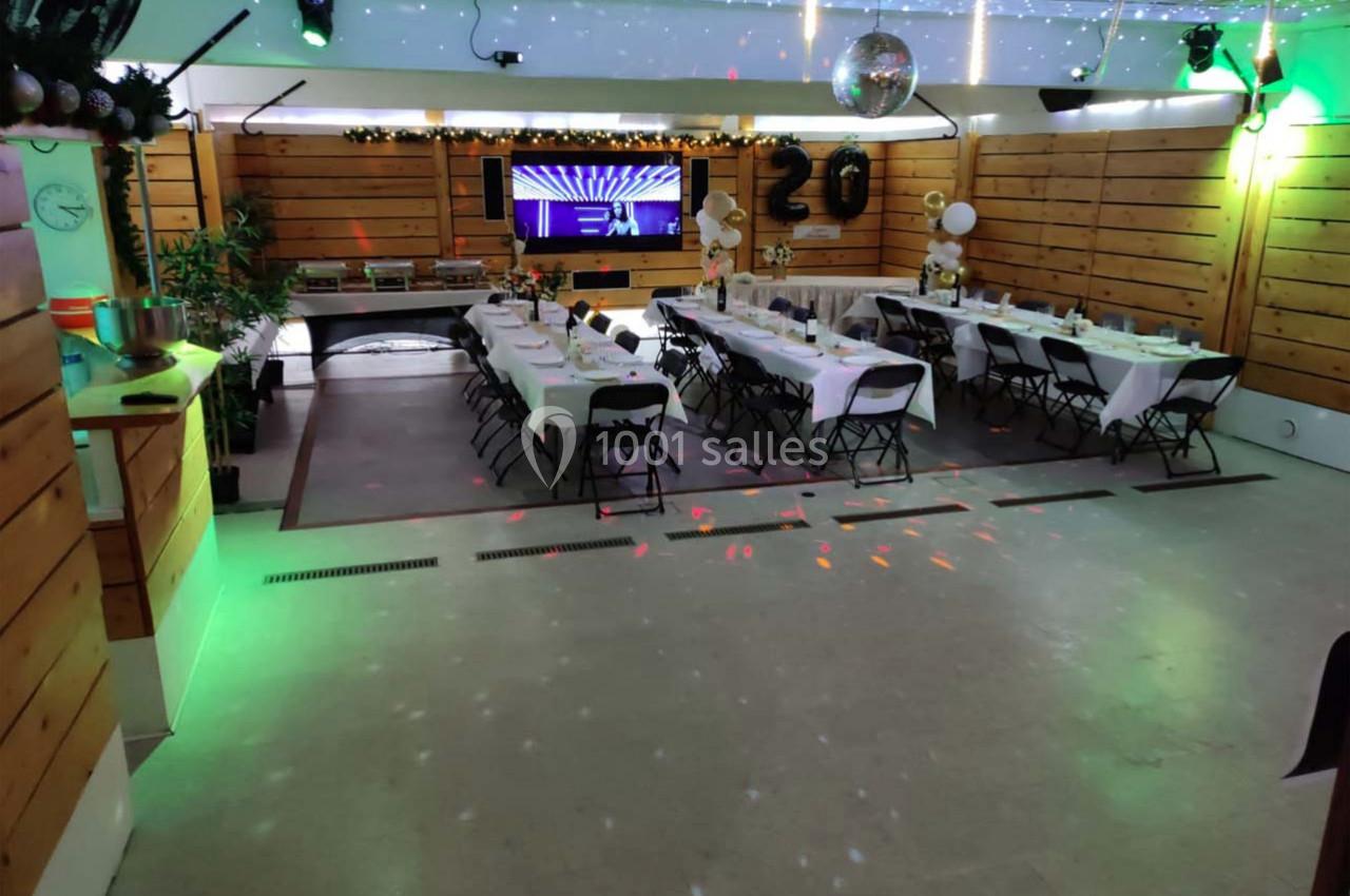 Salle décorée pour un événement, avec tables dressées, chaises pliantes et éclairage festif.