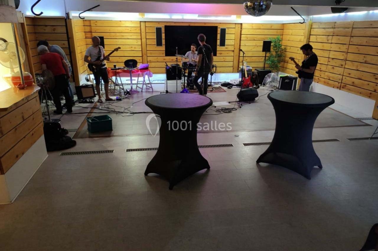 Musiciens installant leur matériel sur une scène dans une salle en bois avec tables hautes au premier plan.