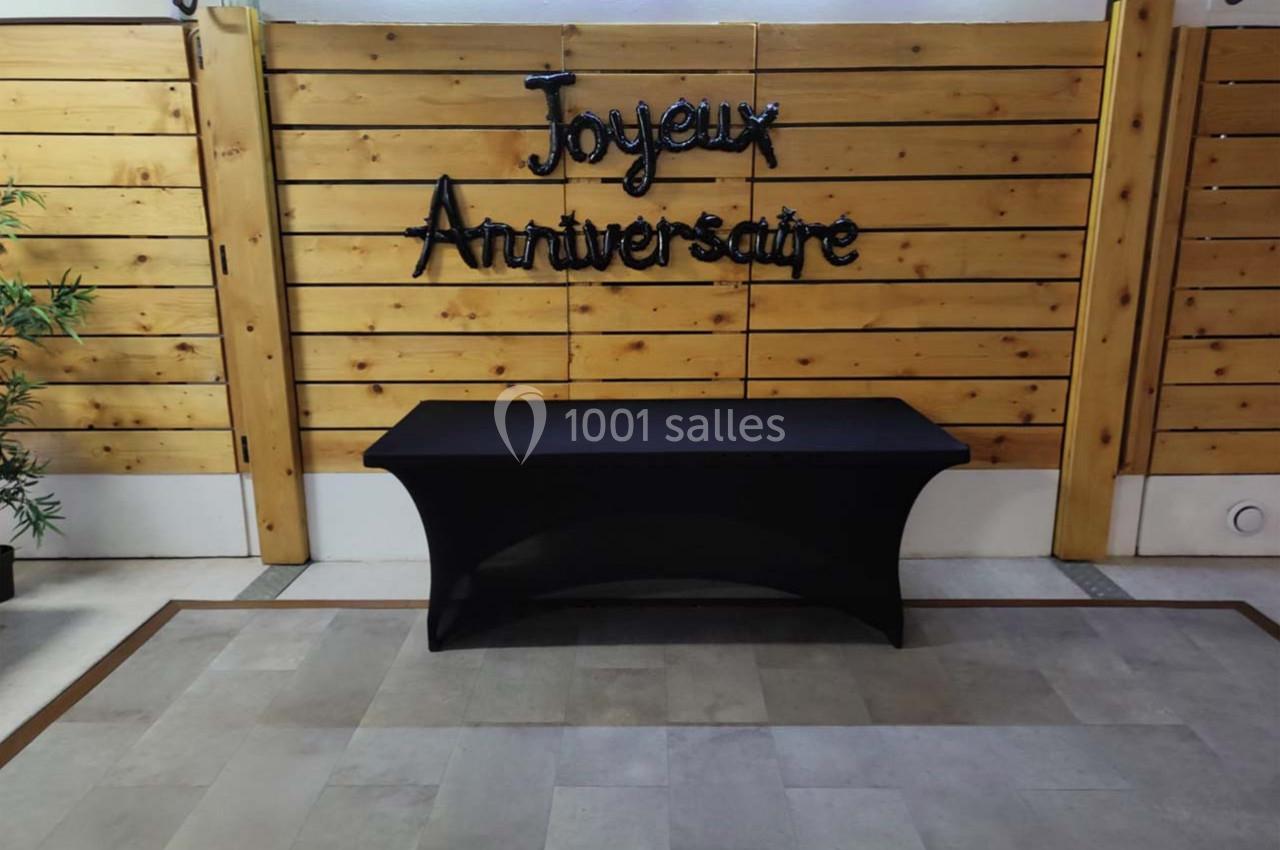 Mur en bois décoré avec l'inscription ’Joyeux Anniversaire’ et une table noire recouverte d'une nappe devant.