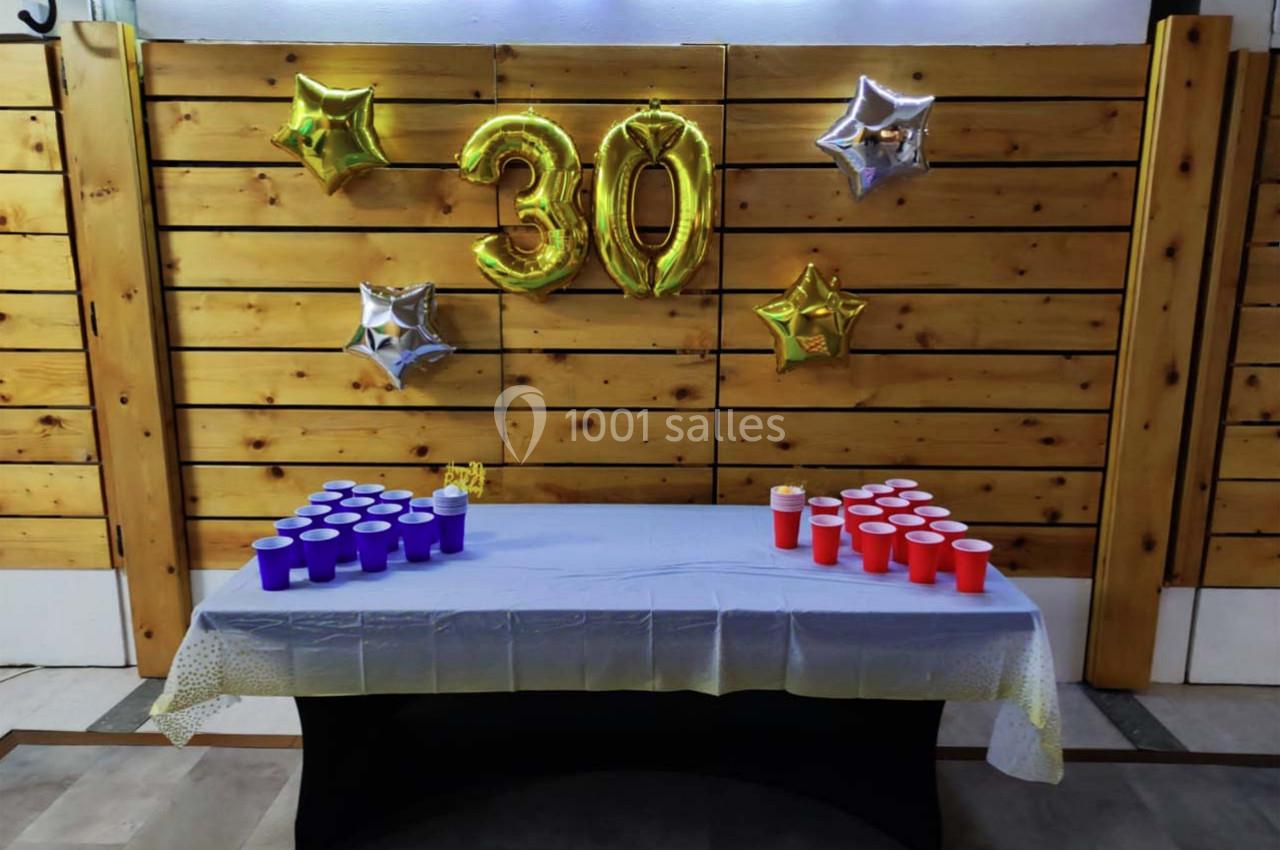 Ballons dorés formant le chiffre 30 accrochés à un mur en bois, avec une table dressée pour un jeu de gobelets colorés.